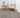 Living room with a gray rug, white armchair, wooden side table, and plant.