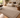 Caramel textured rug with a subtle bordered design and overlocked edges, styled in a modern living room with a cream sofa, wooden coffee table and timber flooring.