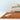 Warm rust rug with an open book on a light gray floor, beige sofa in the background