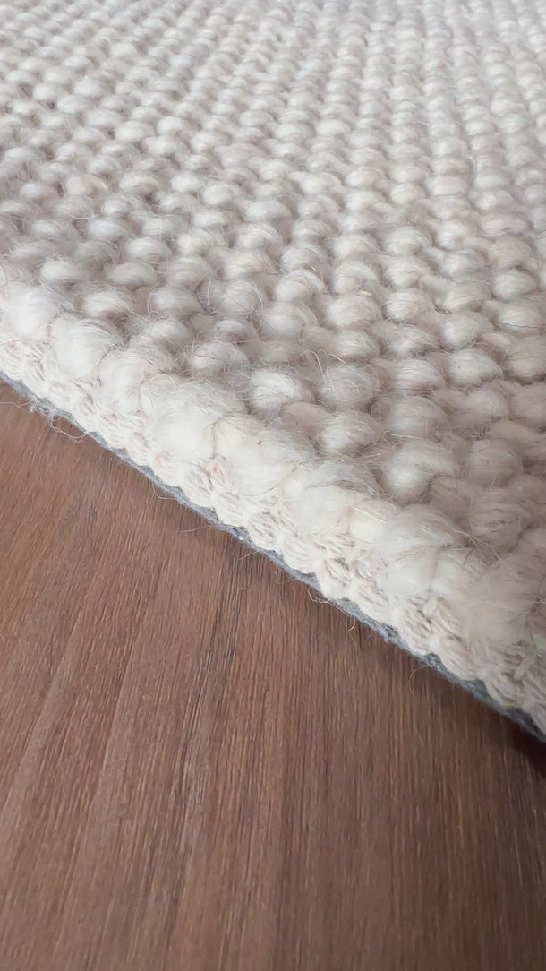 Close-up of Wayanad beige wool rug on floorboards in natural light.